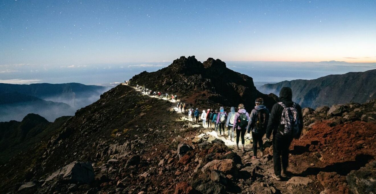 Randonneurs équipés de frontales gravissant le sentier volcanique du Piton des Neiges sous les étoiles avec vue panoramique