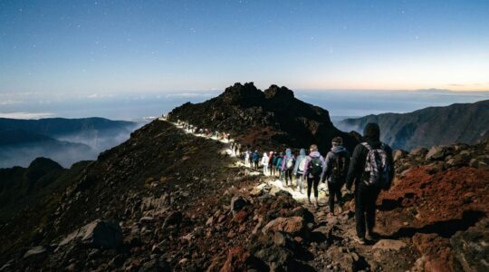Randonneurs équipés de frontales gravissant le sentier volcanique du Piton des Neiges sous les étoiles avec vue panoramique
